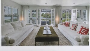 Een ruime woonkamer met een groot raam, een bank, een salontafel en een open deur naar een balkon.