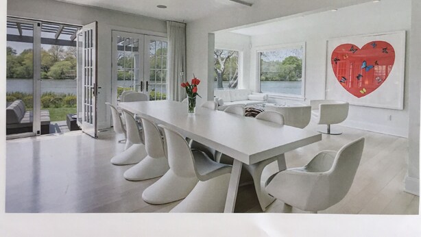 Een moderne eetruimte met een lange tafel, witte stoelen en uitzicht op een meer door grote ramen.