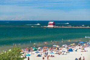 A beach with a lighthouse, boats, and a pier.