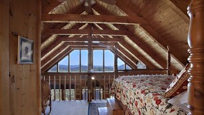 A high-ceilinged room with a wooden ceiling and a large bed with floral bedding. - Top-of-Mountain Cabin w/ Views, Hot Tub & Game Room – Near Pigeon Forge (Sevierville)