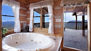 A wooden cabin with a large bathtub, lace curtains, and a view of mountains. - Top-of-Mountain Cabin w/ Views, Hot Tub & Game Room – Near Pigeon Forge (Sevierville)