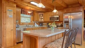 A kitchen with wooden cabinets, a granite countertop, stainless steel appliances, and a bar stool. - Top-of-Mountain Cabin w/ Views, Hot Tub & Game Room – Near Pigeon Forge (Sevierville)
