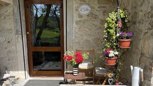 A stone porch with a wooden door, a small table with a chair, and potted plants.