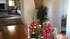 A wooden dining table with a bottle of wine, a vase with flowers, and candles.
