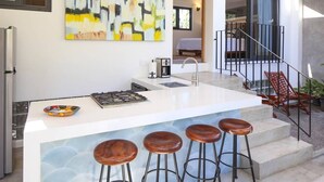 Une cuisine moderne avec un îlot central blanc, des tabourets de bar et un tableau accroché au mur.
