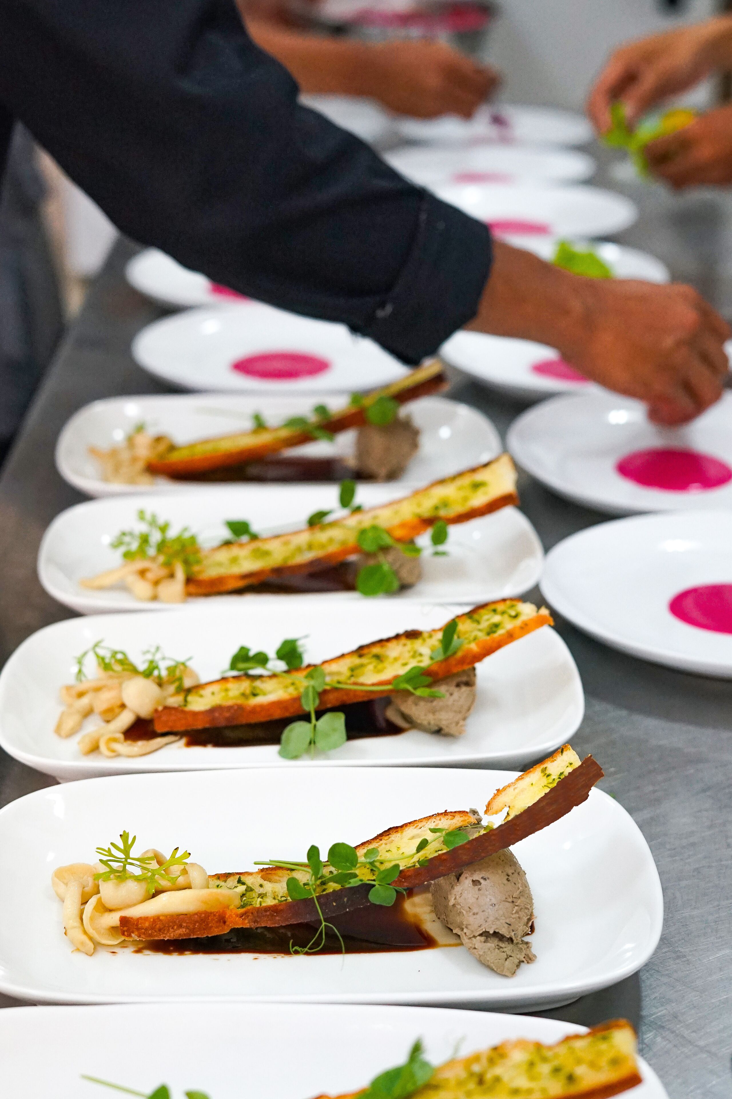 A row of white plates with food, each garnished with green herbs.