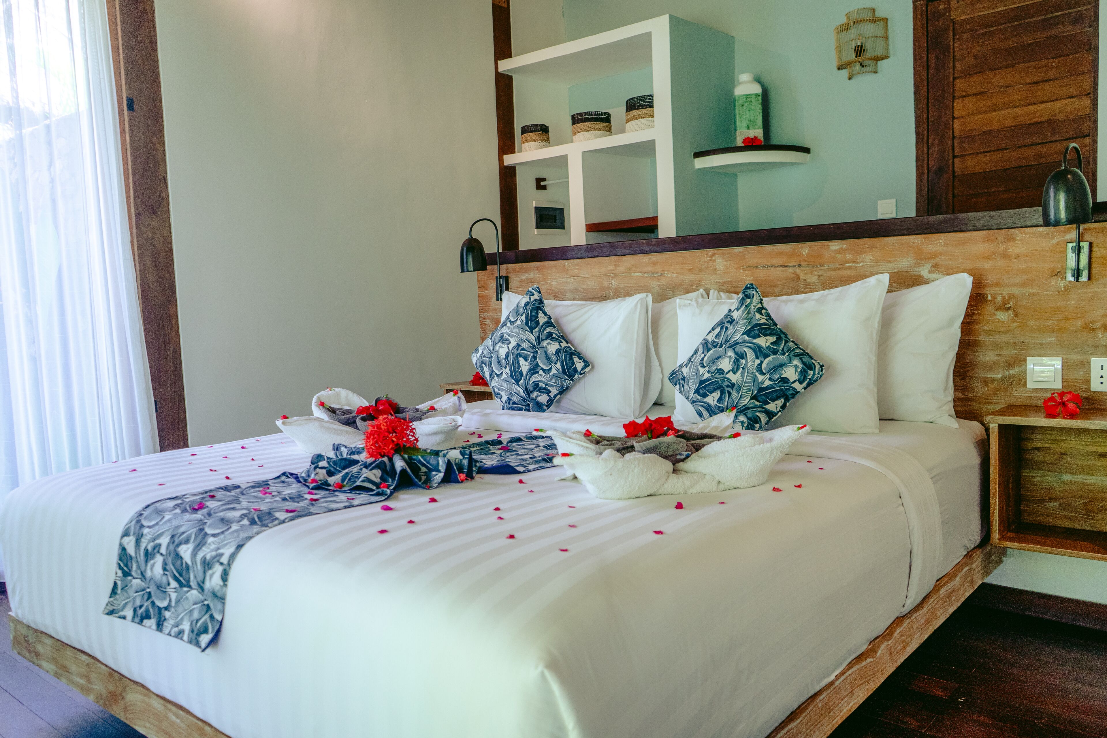 A neatly made bed with a floral-patterned blanket, blue and white pillows, and red flowers.