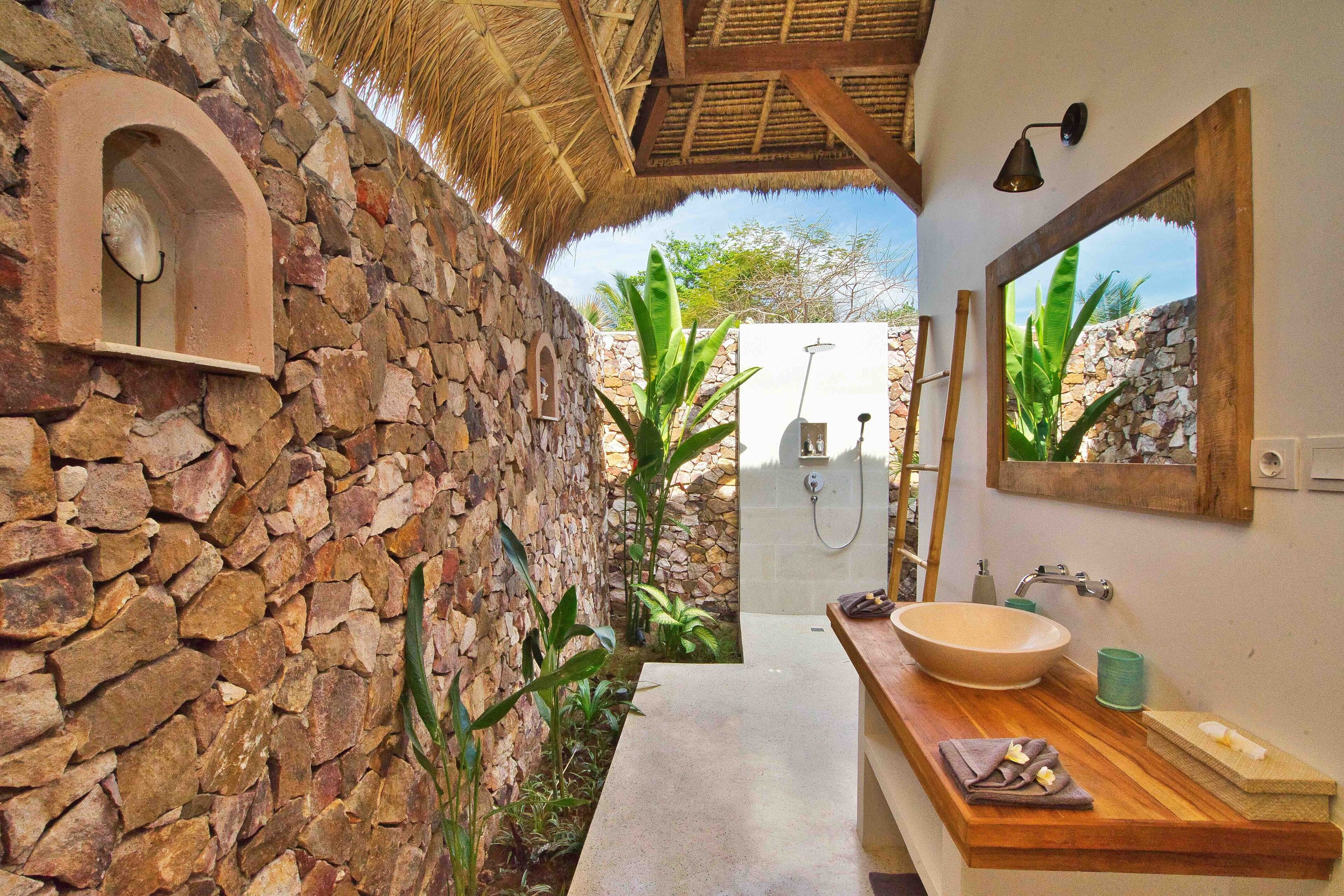 A bathroom with a stone wall, a wooden vanity, a large mirror, and a shower area.