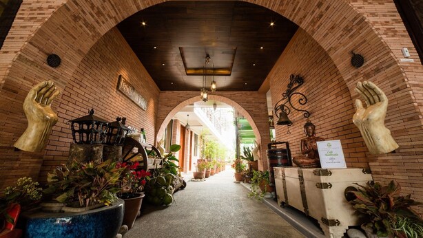 A brick-walled corridor with a central archway, potted plants, and a vintage suitcase on the right. - Gwandalan House (Dipolog)