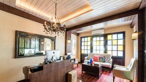 A hotel lobby with a reception desk, a chandelier, a large mirror, and a sofa with colorful cushions. - Gwandalan House (Dipolog)