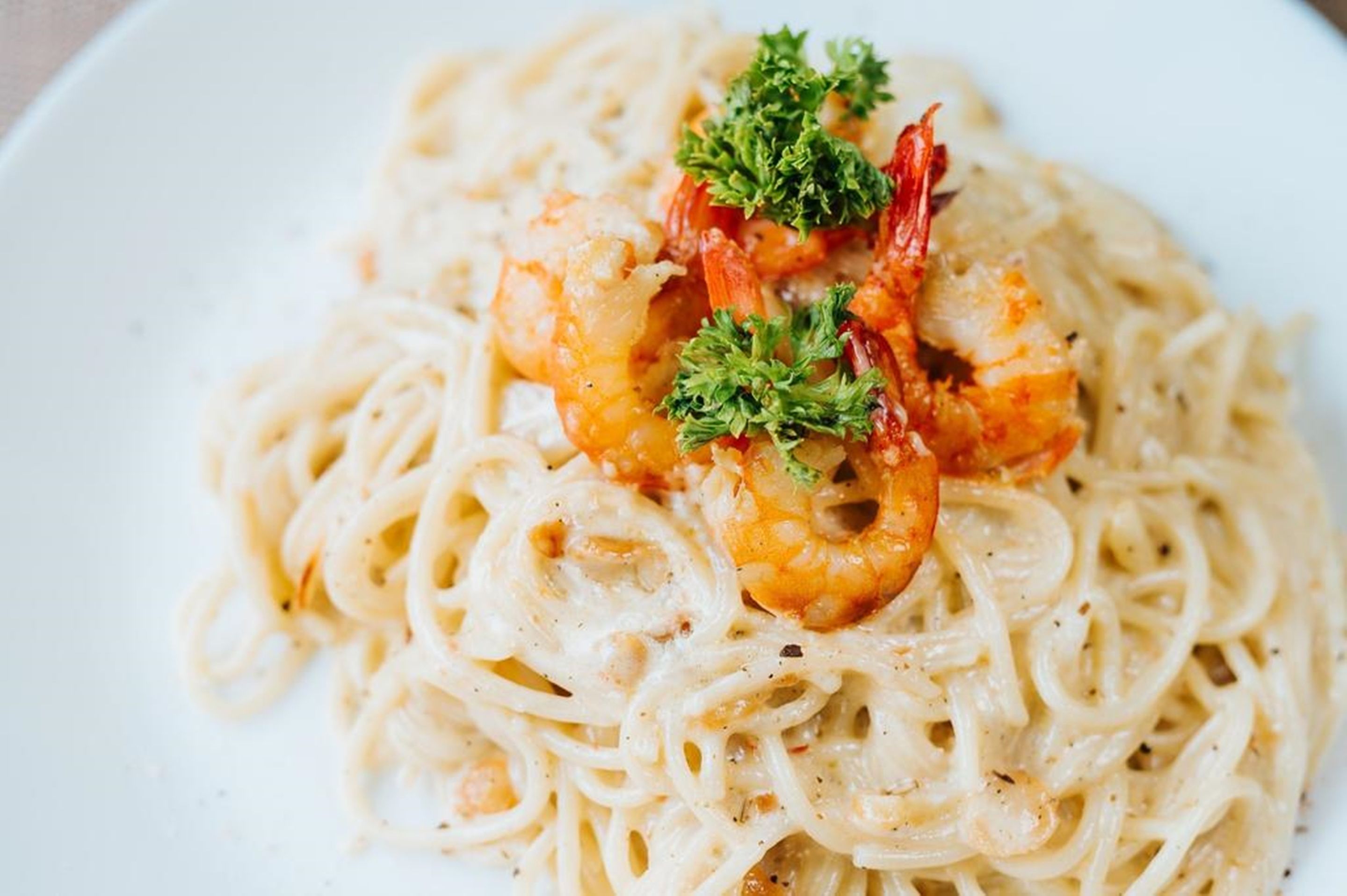 A plate of spaghetti with shrimp and parsley garnish.