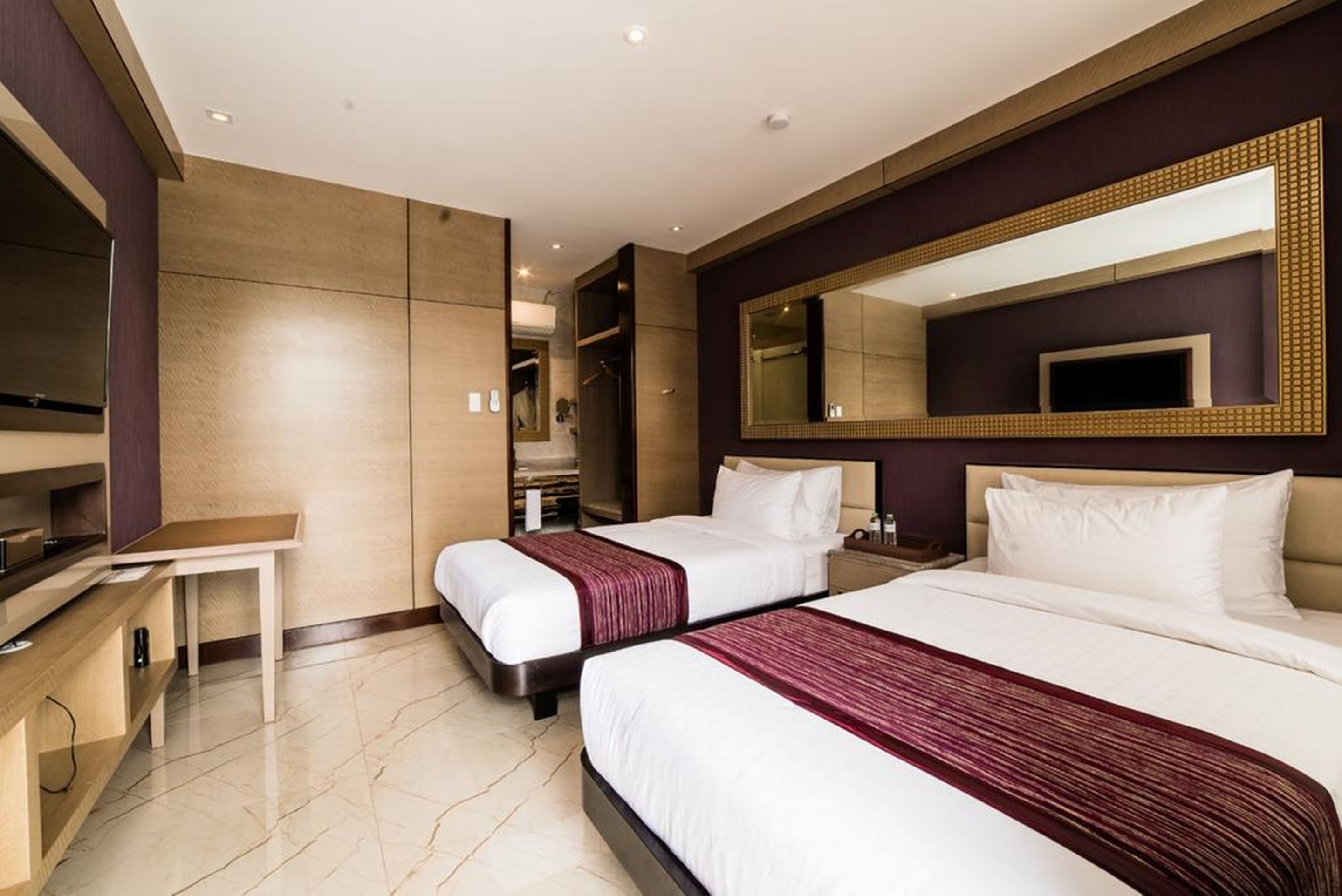 A hotel room with two beds, a TV, a desk, and a large mirror.