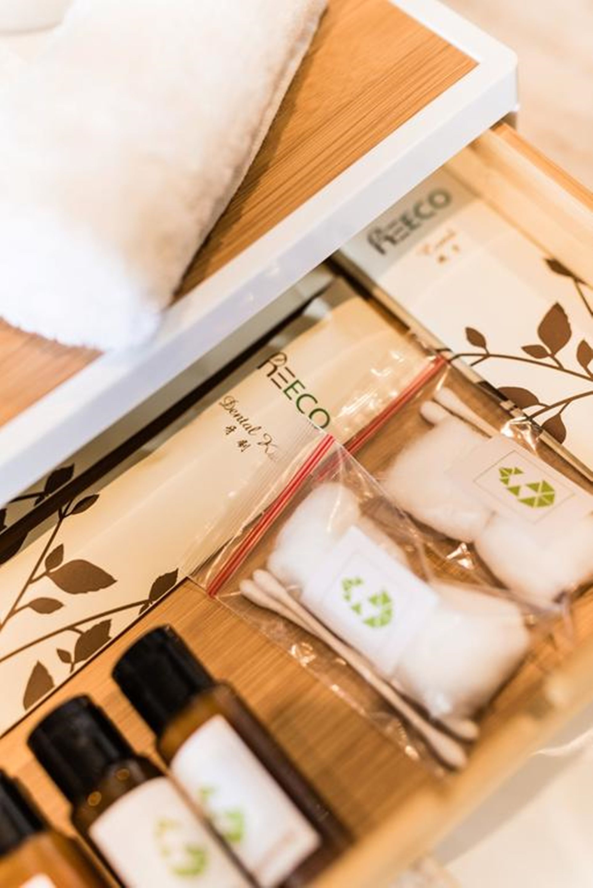 Una bandeja de madera con varios objetos, entre ellos un almohadón blanco, una caja con la etiqueta 'RECO' y varias botellas pequeñas.