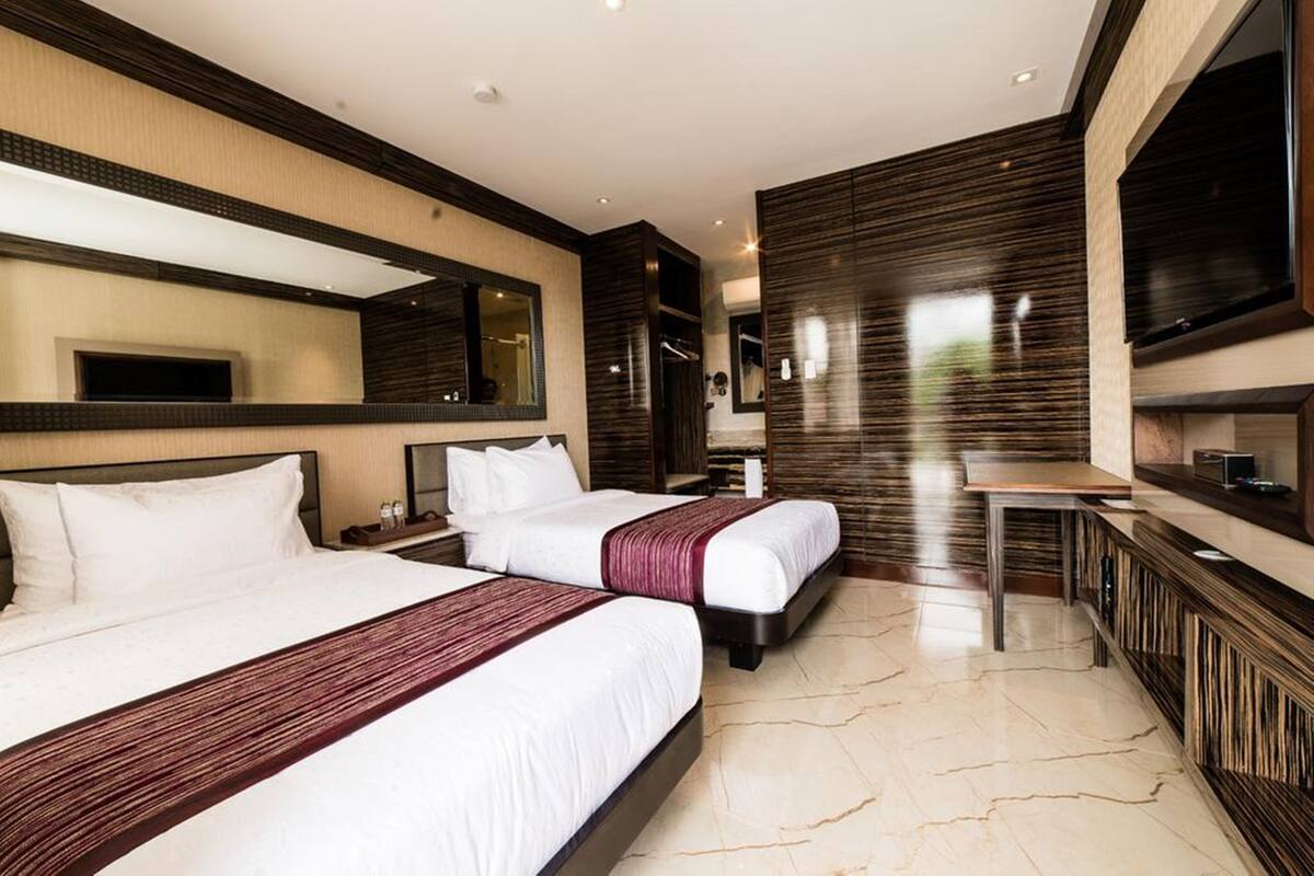 A modern hotel room with two beds, a large mirror, a flat-screen TV, and a marble floor.