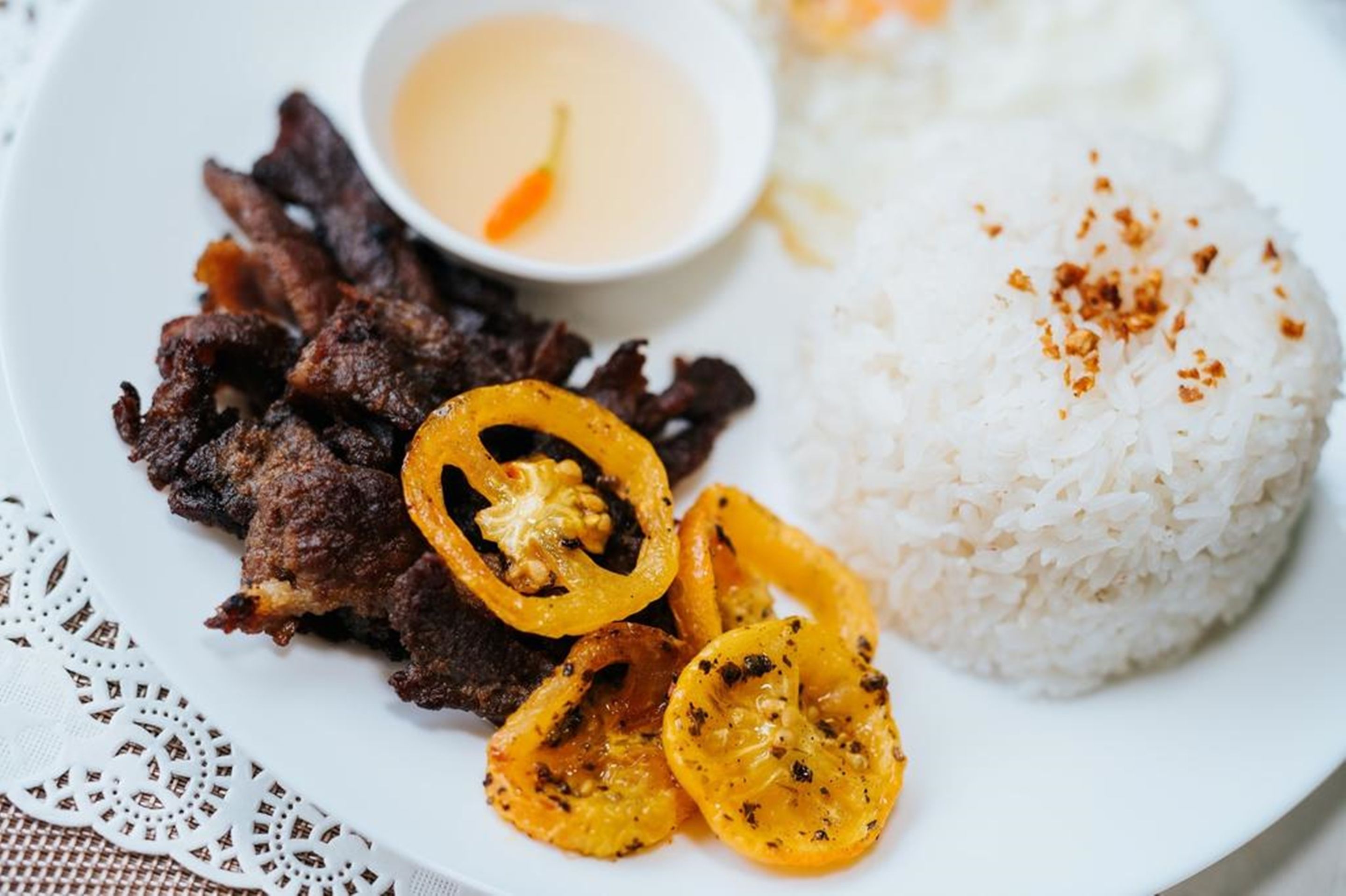 A plate with grilled meat, sliced bell peppers, and white rice, accompanied by a small bowl of sauce.