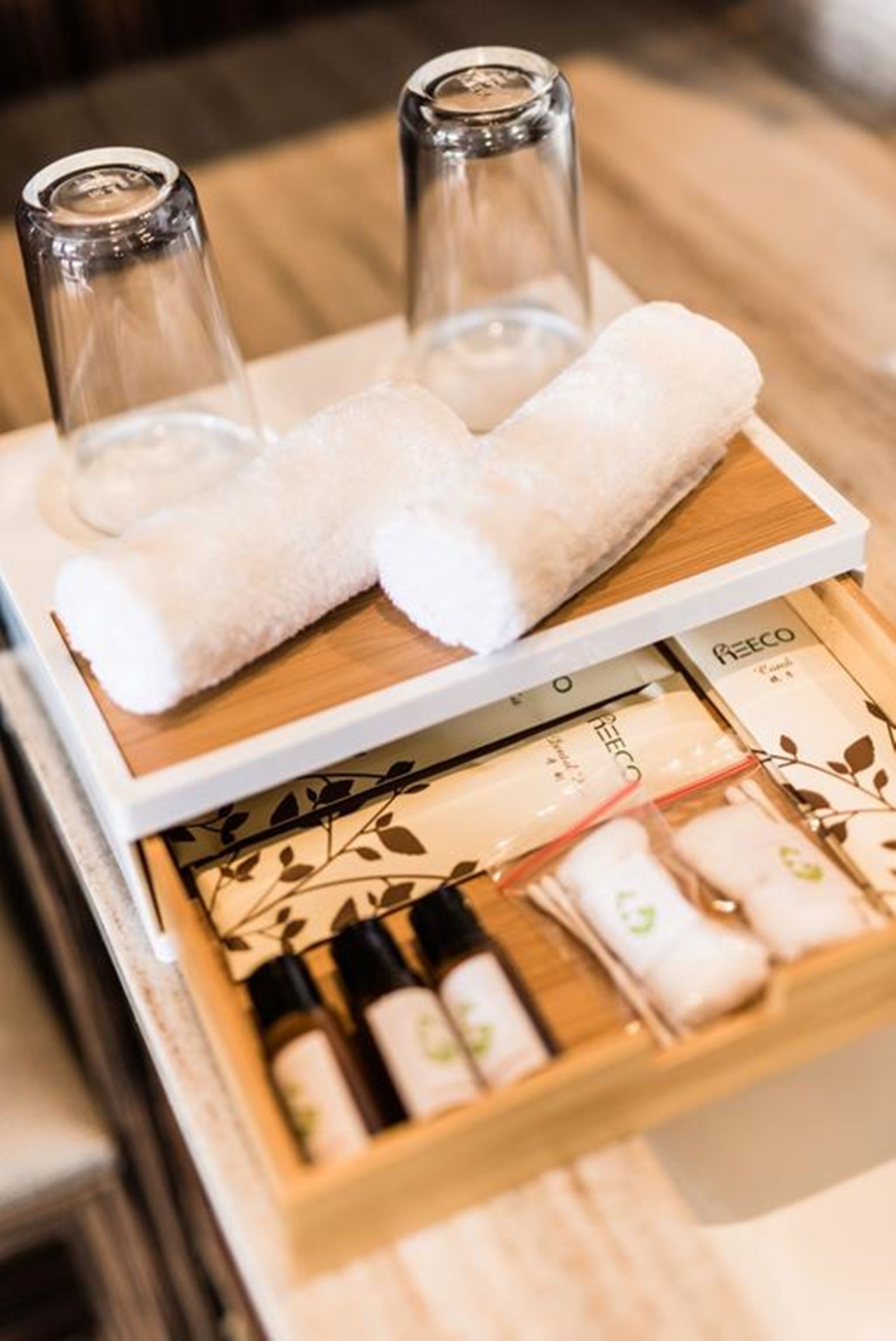 A wooden tray with three white towels and a set of bottles, likely containing toiletries, on a wooden surface.
