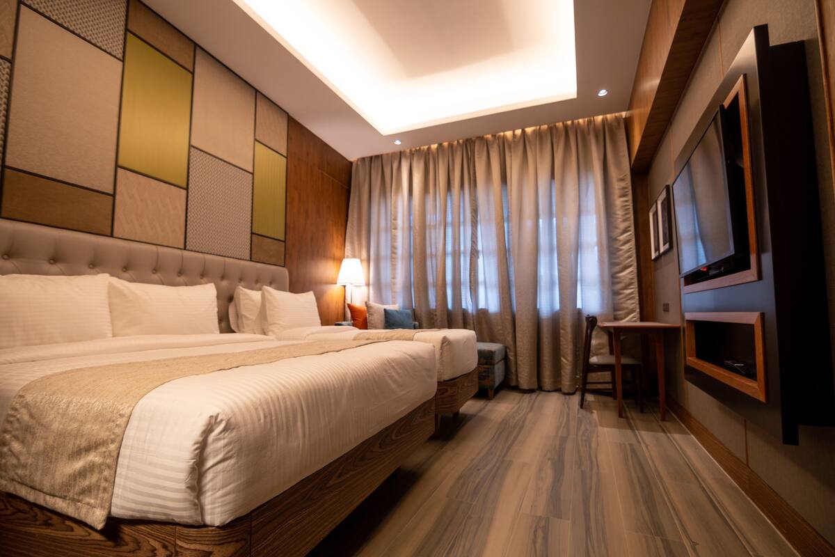 A hotel room with a large bed, a desk, a TV, and a window with curtains.