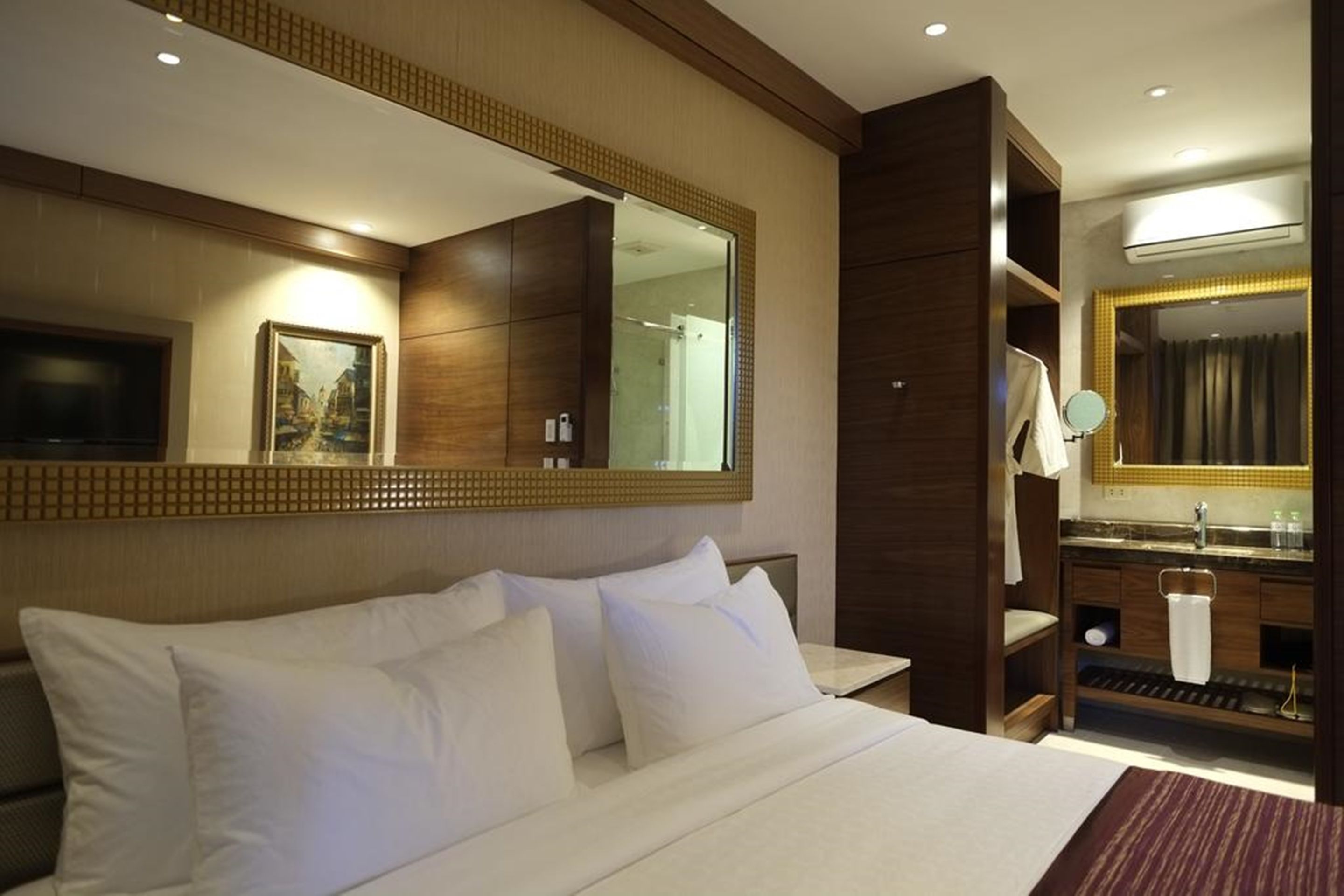 Una habitación de hotel con una cama grande, un espejo, un tocador con lavabo y un televisor.