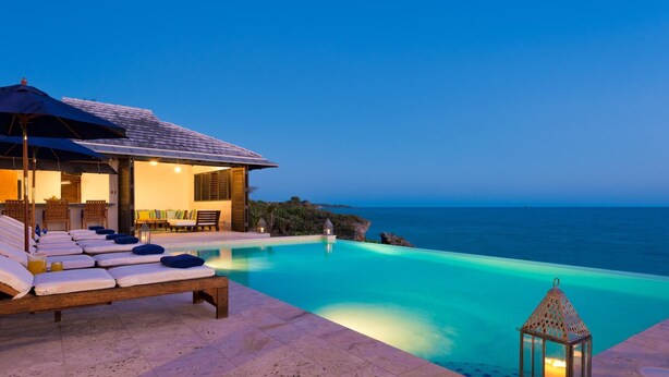 Área junto à piscina com espreguiçadeiras e um candeeiro, com vista para um oceano azul e límpido.
