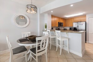 Una cocina moderna con armarios blancos, una isla central y un comedor con sillas blancas y una mesa redonda.