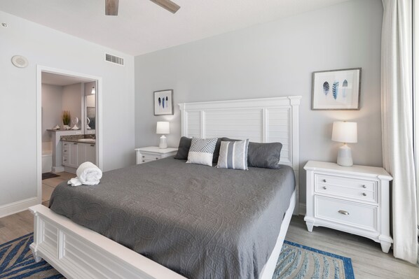 Une chambre à coucher bien rangée, avec un lit, des tables de chevet, une commode et une salle de bain visible à travers une porte ouverte.