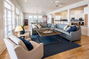 A spacious living room with a grey sectional sofa, a coffee table, and a lamp. There is a view of the kitchen and dining area through an open doorway. - Semper Fi Grayton gulf front 3bedroom, 3 bath On Gulf (Santa Rosa Beach)