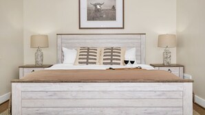 A bed with a wooden headboard, two bedside tables with lamps, a framed picture on the wall, and two wine glasses on the bed.