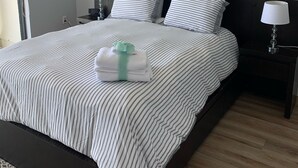 Una cama bien hecha con ropa de cama a rayas, dos cuadros colgados en la pared, un ventilador de techo, lámparas de noche y una mesita de noche pequeña.