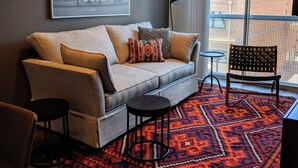 A modern living room with a grey sofa, patterned cushions, a black floor lamp, and a red and black rug.