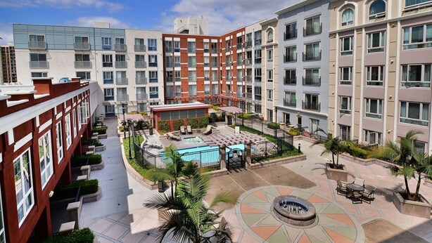 A multi-story hotel with a central courtyard featuring a swimming pool, outdoor seating, and palm trees.