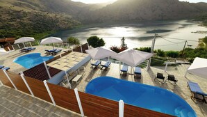 A pool area with lounge chairs and umbrellas, overlooking a lake with mountains in the background. - Villa by the Lake with 2 Newly Built Private Pool (Georgioupolis)