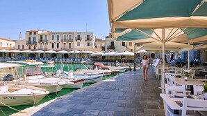 A marina with boats docked, a woman walking, and outdoor seating with umbrellas. - Villa by the Lake with 2 Newly Built Private Pool (Georgioupolis)