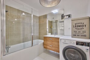 Bany modern amb plat de dutxa de vidre, rentamàquina integrada i un lavabo amb mirall.