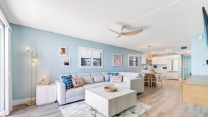 A modern living room with a white sofa, a coffee table, and a dining area with a table and chairs.