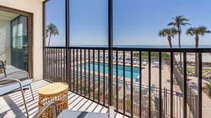 A balcony with a view of a pool and beach, featuring a table and chairs.