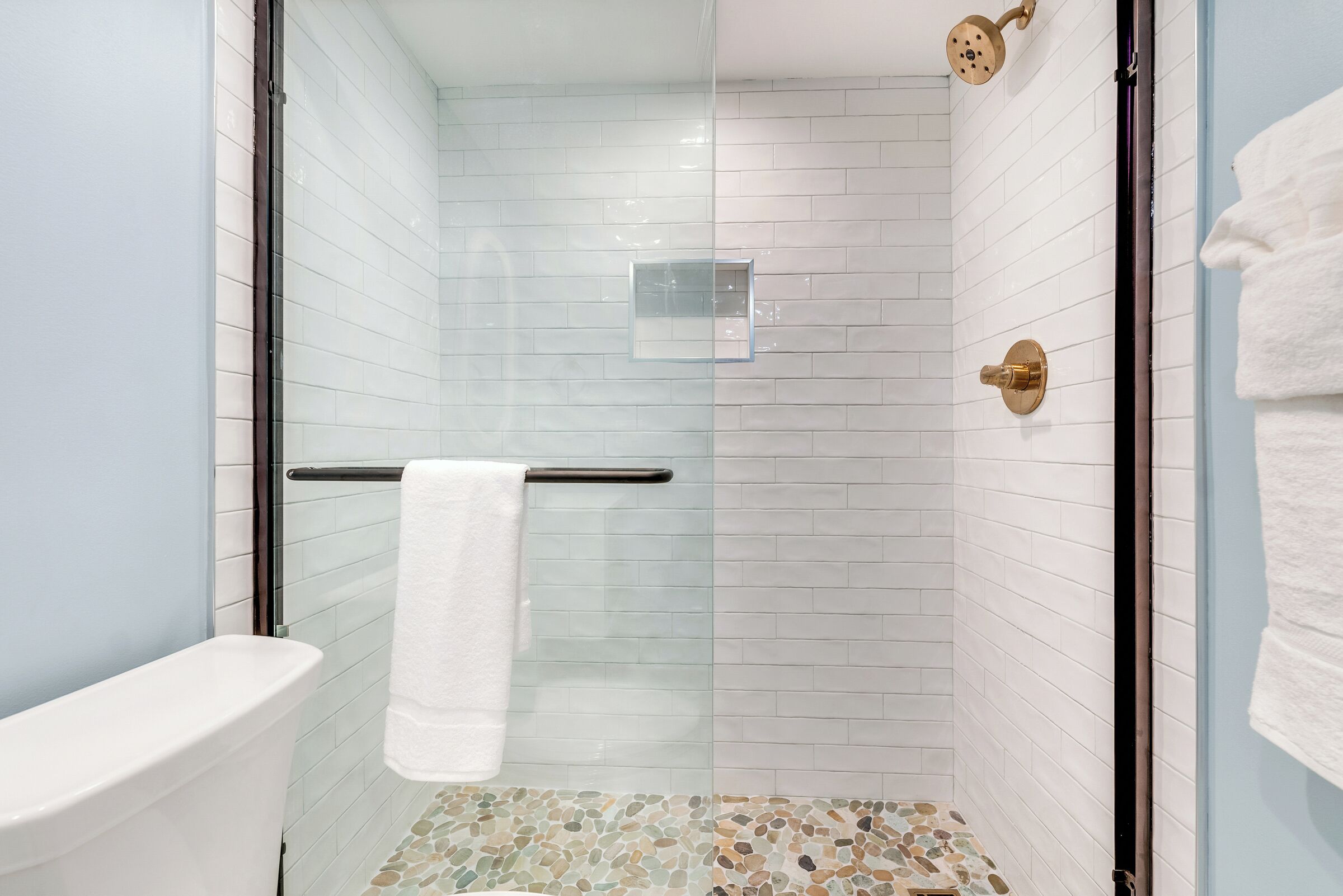 A shower with a glass door, a white tiled wall, and a mosaic floor.
