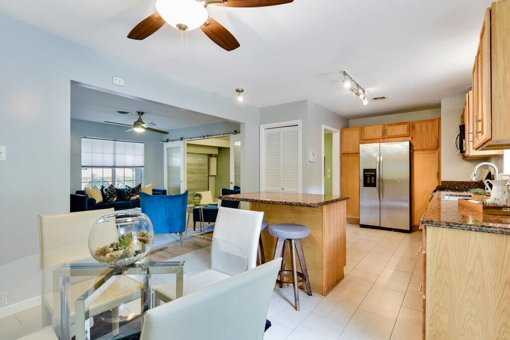 A modern kitchen with a central island, wooden cabinets, and a stainless steel refrigerator.