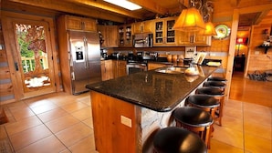 A spacious kitchen with wooden cabinets, a large island with stools, stainless steel appliances, and a decorative ceiling light. - Mtn Views-4BR-GameRm-More! (Sevierville)