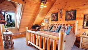 A wooden cabin bedroom with a sloped ceiling, a bed with patterned bedding, and wall-mounted animal head decorations. - Mtn Views-4BR-GameRm-More! (Sevierville)