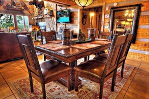 Cozy dining area with a large table for six, surrounded by matching chairs, a stone fireplace, and a television.