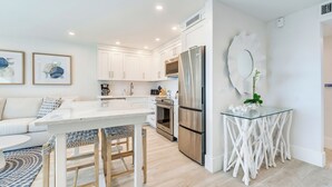 A modern kitchen with white cabinetry, a stainless steel refrigerator, and a glass island.