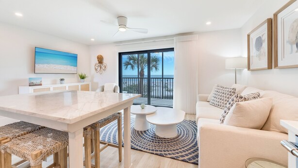 A modern living room with a marble table, a sofa, and a balcony with a view of palm trees.