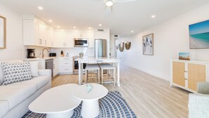 A modern kitchen with white cabinets, a dining area with a white table, and a ceiling fan.
