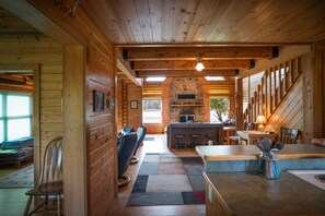 Een blokhutinterieur met een stenen openhaard, houten wanden, een eethoek en een bar.