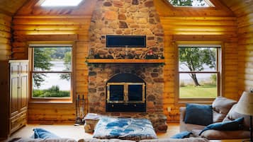 A log cabin with a stone fireplace, wooden walls, and large windows overlooking a lake.