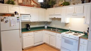 A compact kitchen with white cabinets, a microwave, a coffee maker, and a stove.