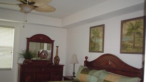Un dormitorio con cama, cómoda, espejo, lámpara y dos cuadros colgados en la pared.