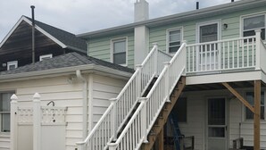 Una casa con fachada blanca, una terraza de madera y una escalera que conduce a un porche cubierto.