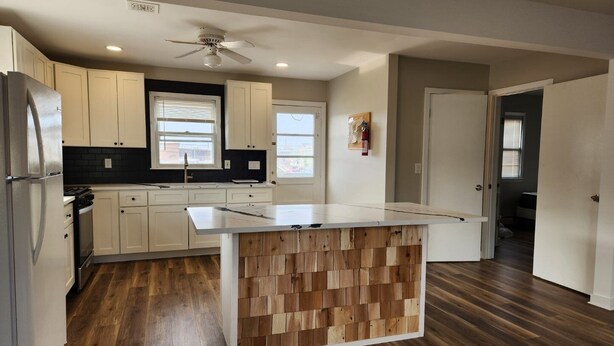 Una cocina moderna con armarios blancos, una isla de madera y un ventilador de techo.