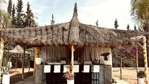 A thatched-roof outdoor bar area with white cushioned chairs and a patterned rug. - Exclusive luxury villa (Marrakesh)